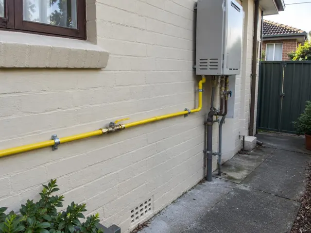 Yellow gas pipe and wall-mounted unit on an exterior brick wall in Cabramatta