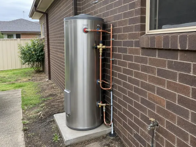 Outdoor hot water cylinder beside a brick wall and window with copper pipework in Canley Vale